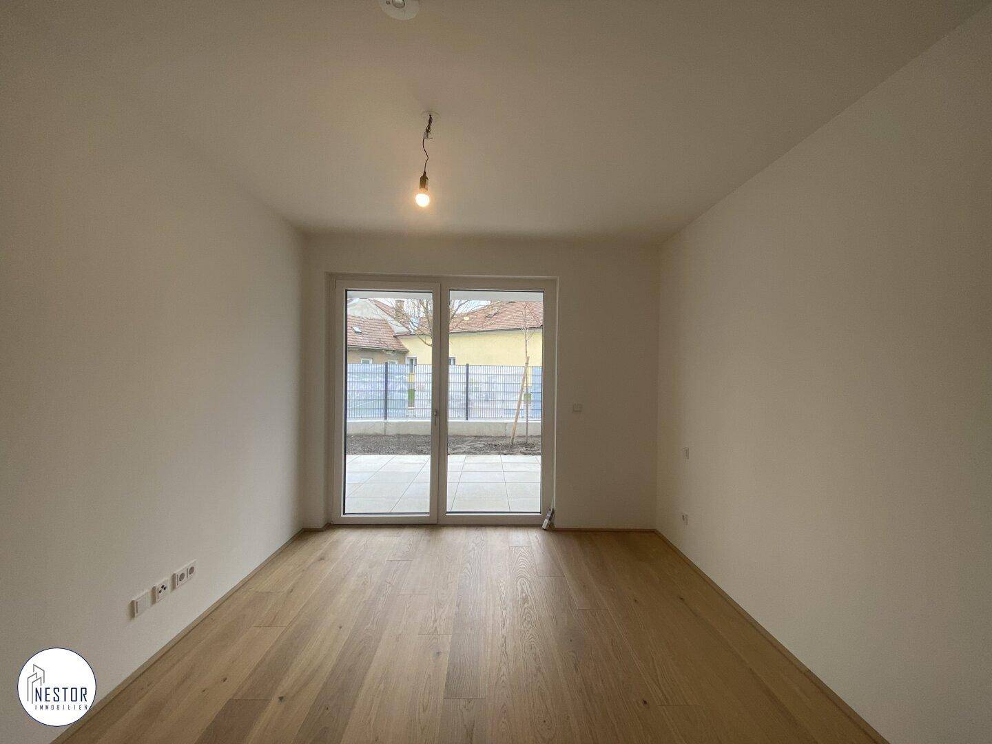 Helles Schlafzimmer mit Holzboden und großen Fenstern, die Zugang zu einem Außenbereich bieten.