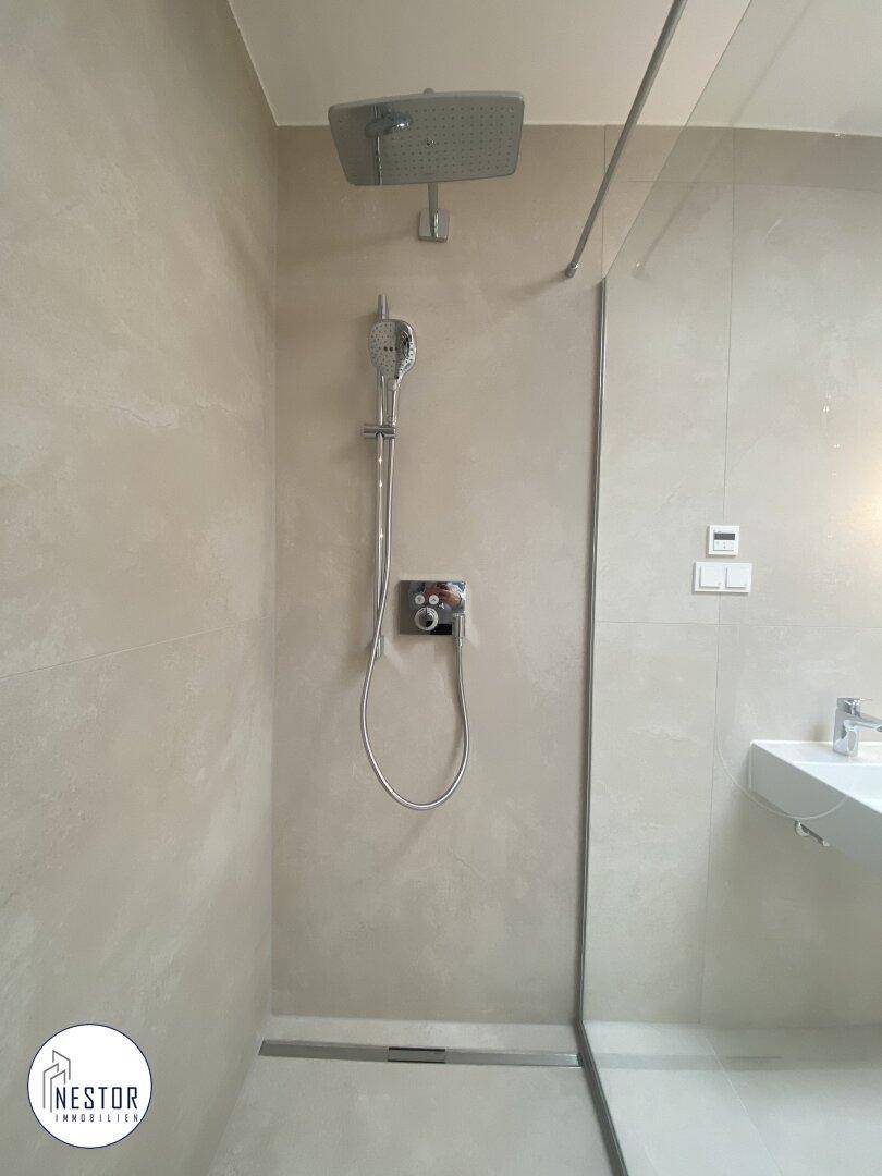 Detailansicht der modernen begehbaren Dusche mit Regenduschkopf und minimalistischen Armaturen.