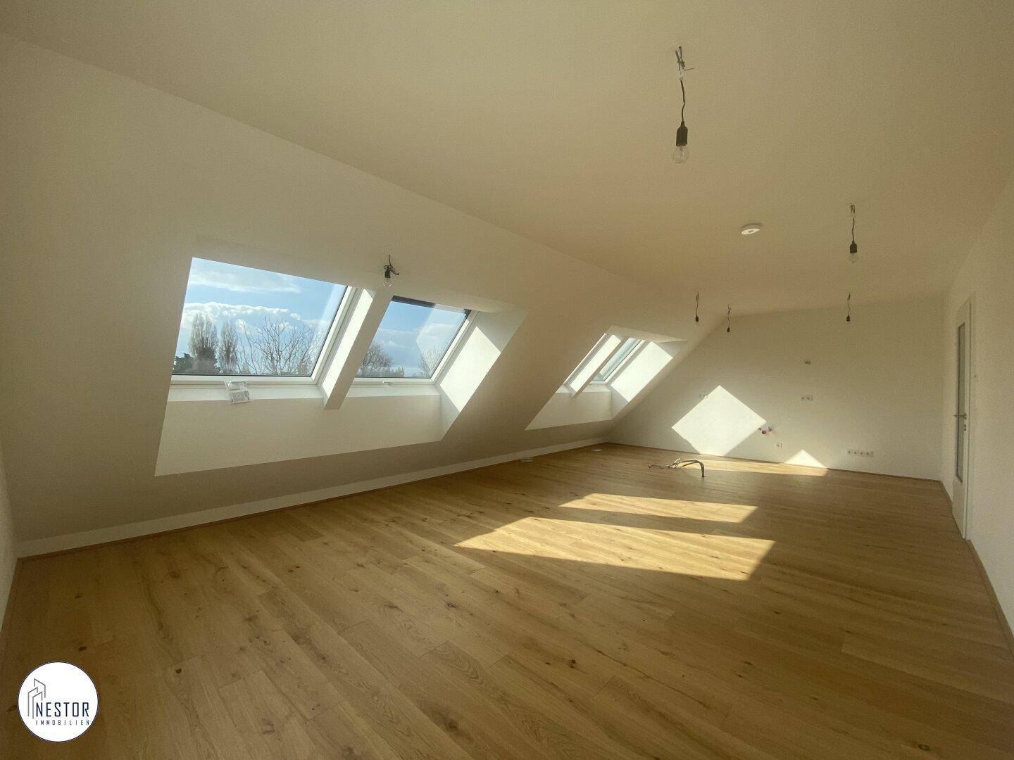 Heller, leerer Raum im Dachgeschoss mit Holzboden und mehreren Dachfenstern für viel Licht.