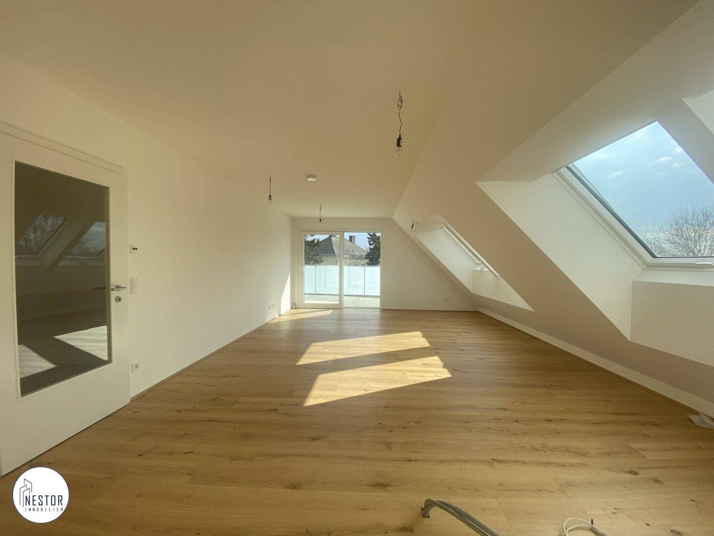 Geräumiger, heller Dachgeschossraum mit Holzboden, Dachfenstern und Zugang zu einem Balkon.