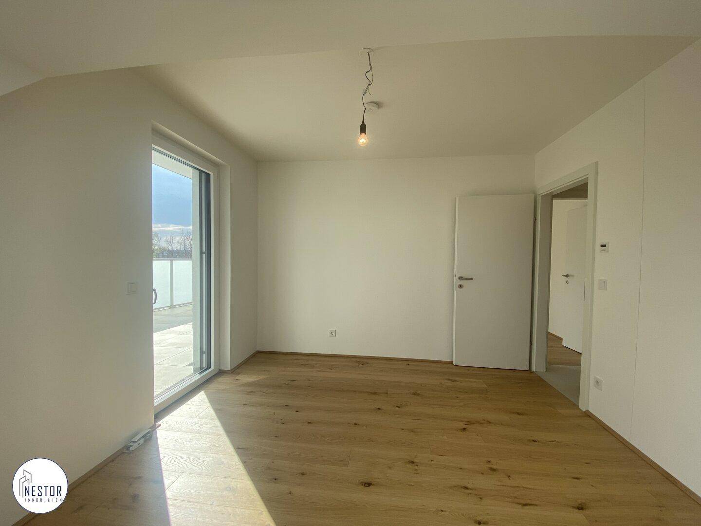 Heller Raum mit Holzboden und großem Schiebetürfenster, das Zugang zu einem Außenbereich bietet.