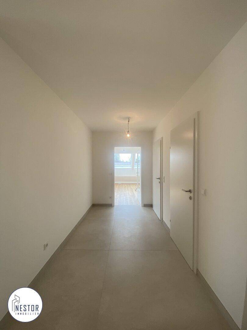 Heller Flur mit Fliesenboden und weißen Türen, der zu weiteren Räumen führt.
