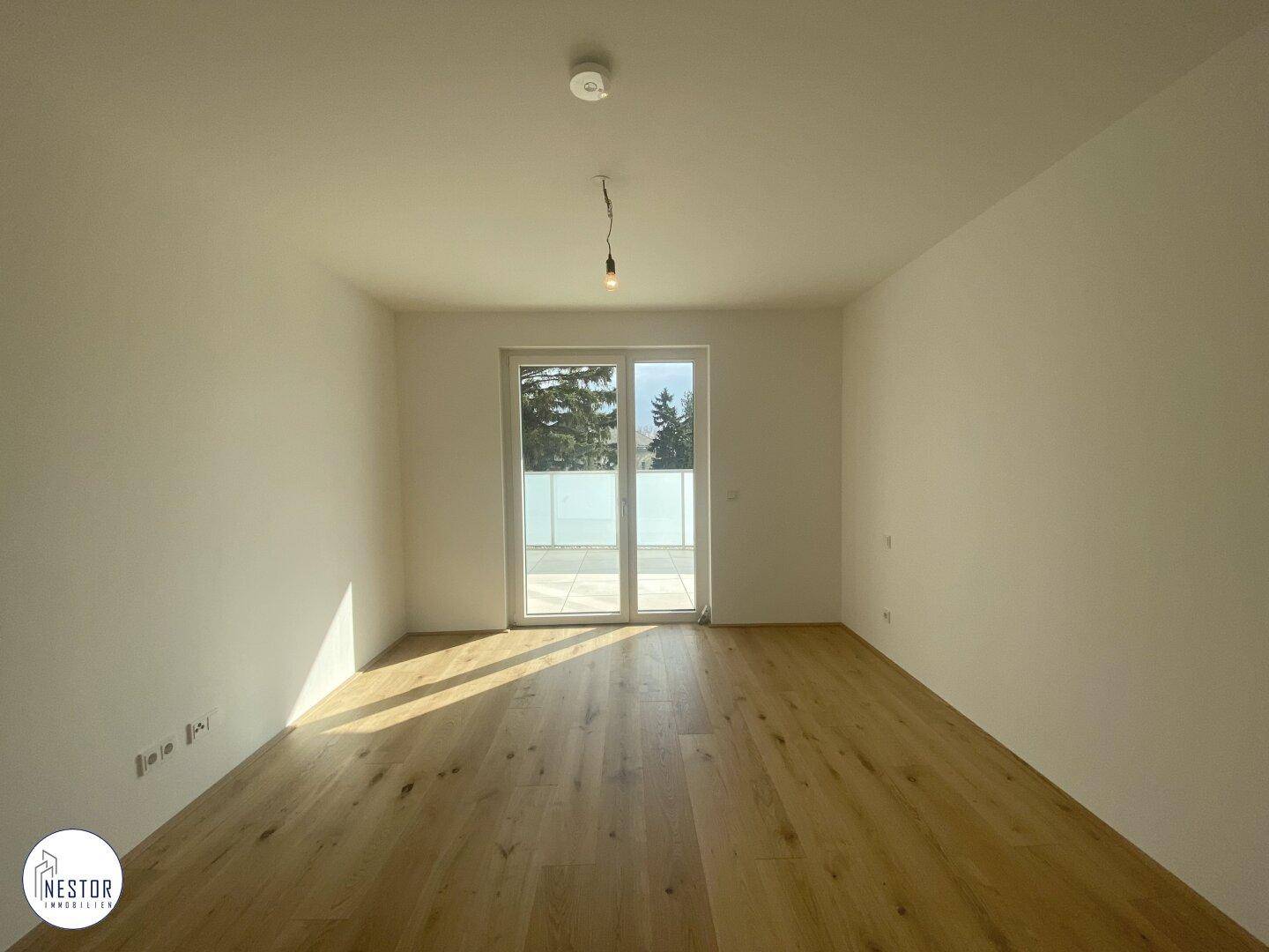 Geräumiger, heller Raum mit Holzboden und Zugang zu einem Balkon durch eine große Glastür.