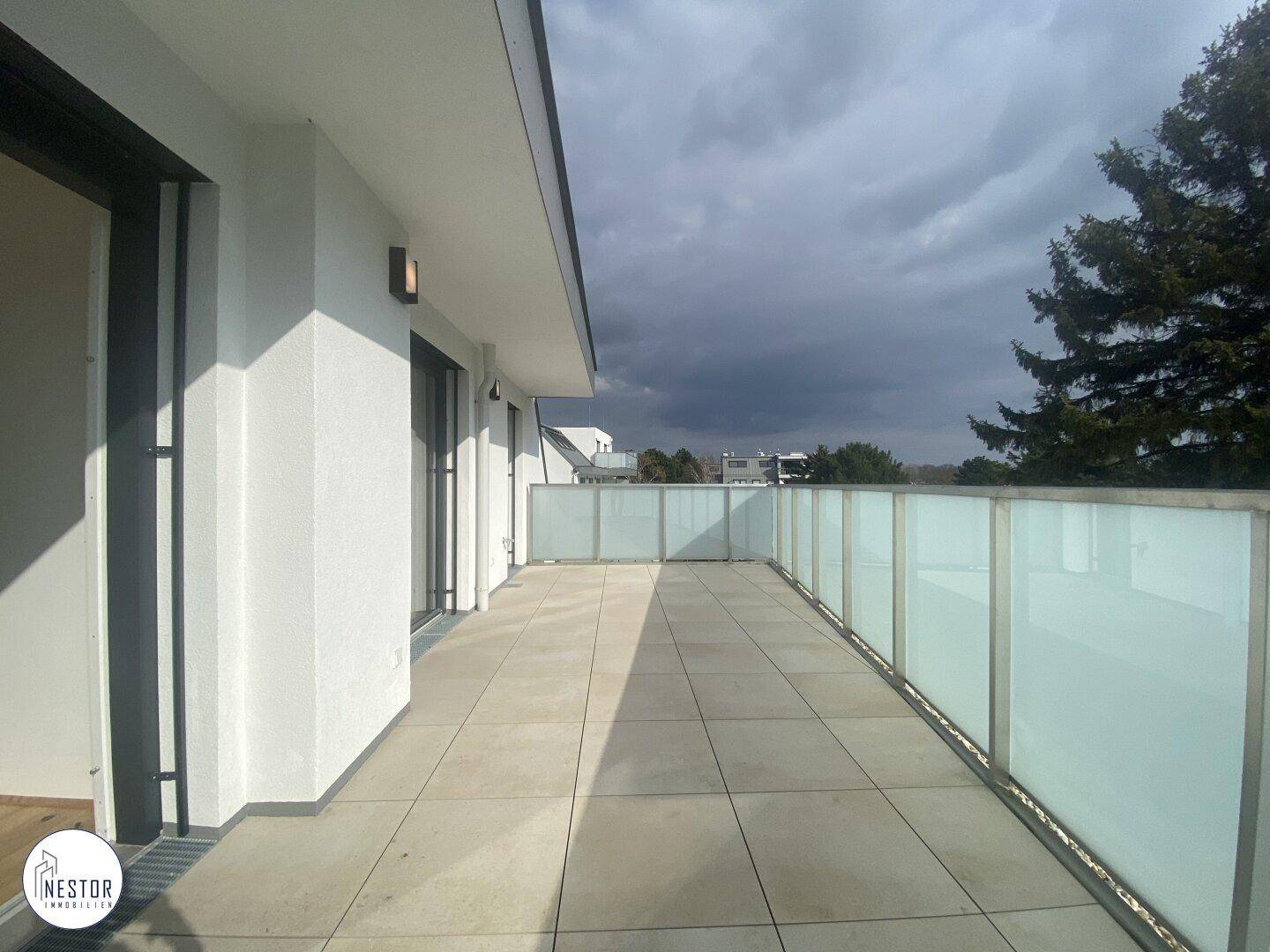 Große, moderne Dachterrasse mit Fliesenboden und Glasgeländer, ideal für Entspannung im Freien.