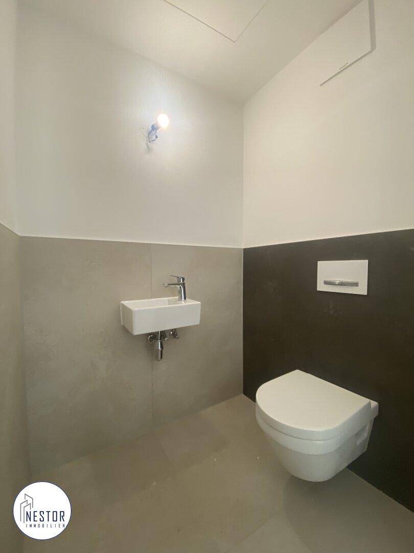Modernes Gäste-WC mit Wand-WC, kleinem Waschbecken und zweifarbiger Wandgestaltung.