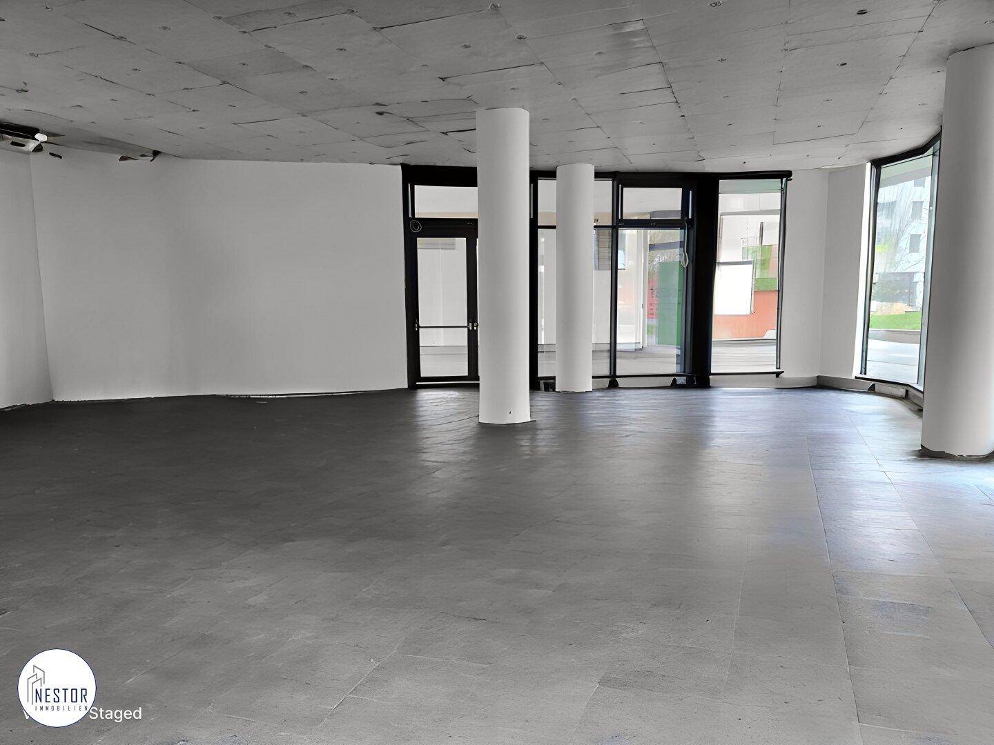 Geräumiger, leerer Gewerberaum im Erdgeschoss mit großen Fenstern und Betonsäulen. Der Boden ist aus poliertem Beton.