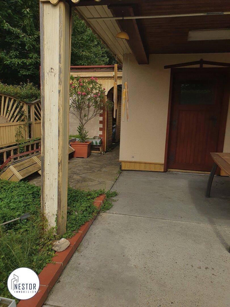 Überdachter Terrassenbereich am Hauseingang mit Holzsäulen und Blick auf den Gartenweg.