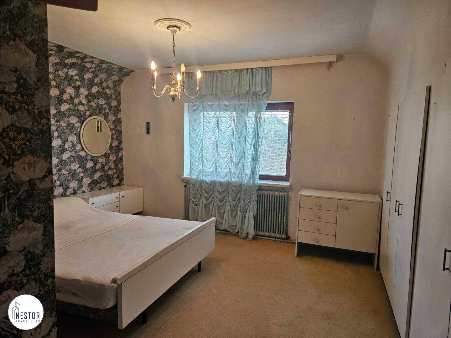 Schlafzimmer mit floraler Tapete, Teppichboden, Kleiderschränken und einem Fenster.