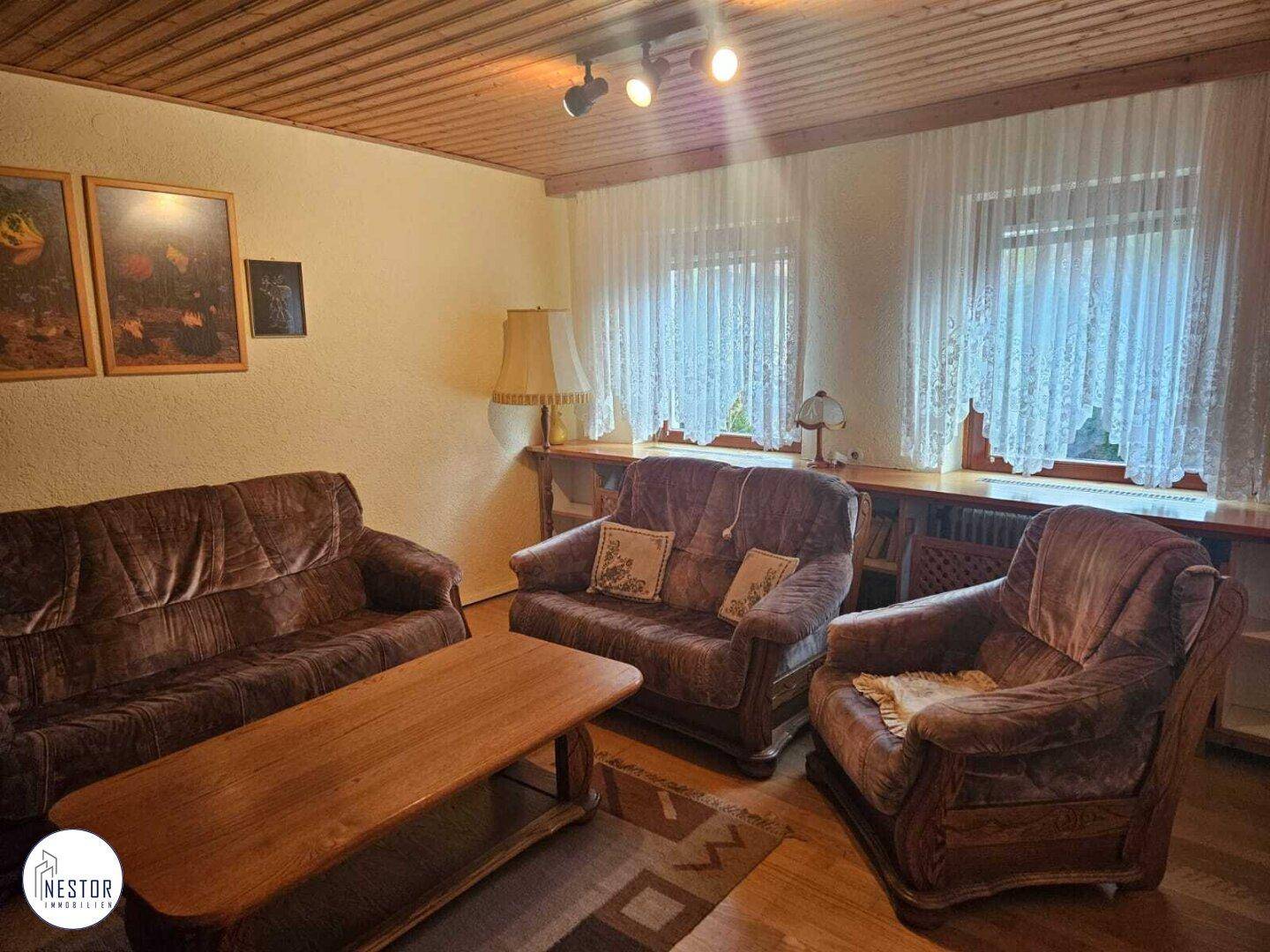 Helles Wohnzimmer mit Holzdecke, bequemen Sofas und einem großen Fenster mit Vorhängen.