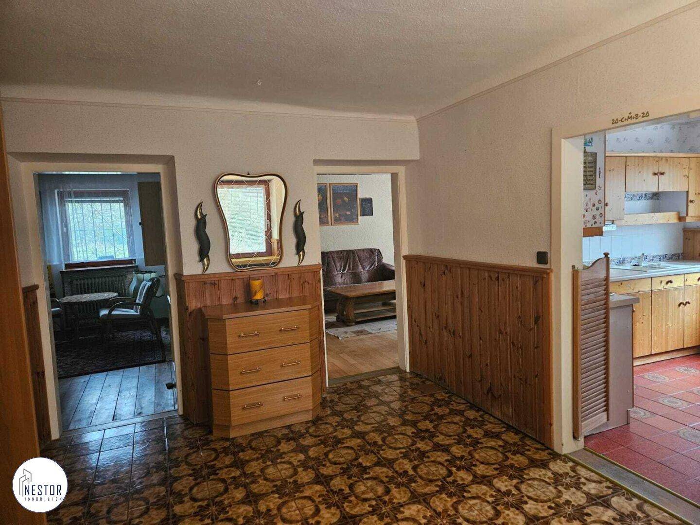 Flur mit gemustertem Fliesenboden, Holzvertäfelung und Zugang zu Küche und Wohnbereich.
