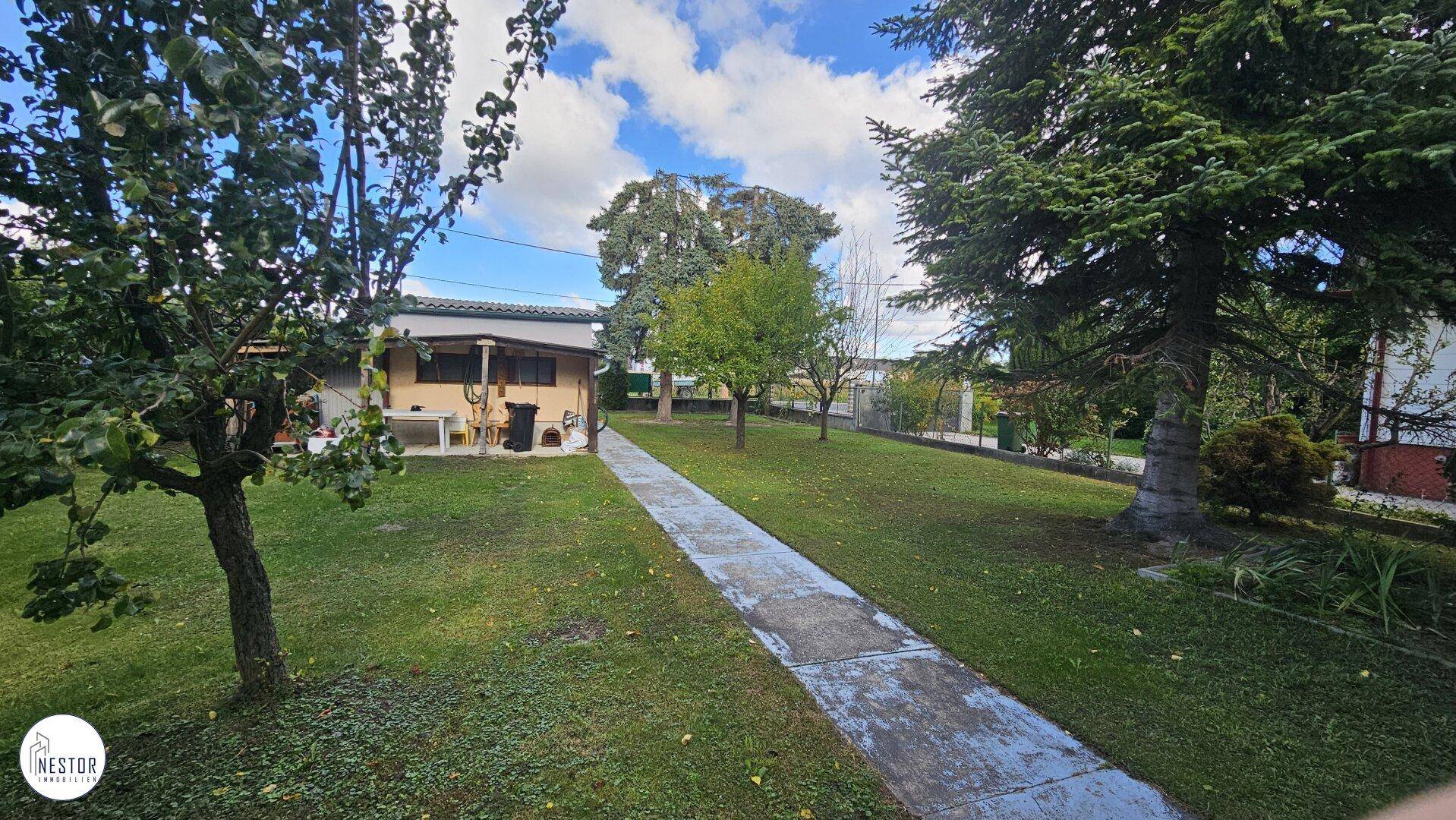 Weitläufiger Garten mit Rasenfläche, altem Baumbestand und einem gepflasterten Weg zum Haus.