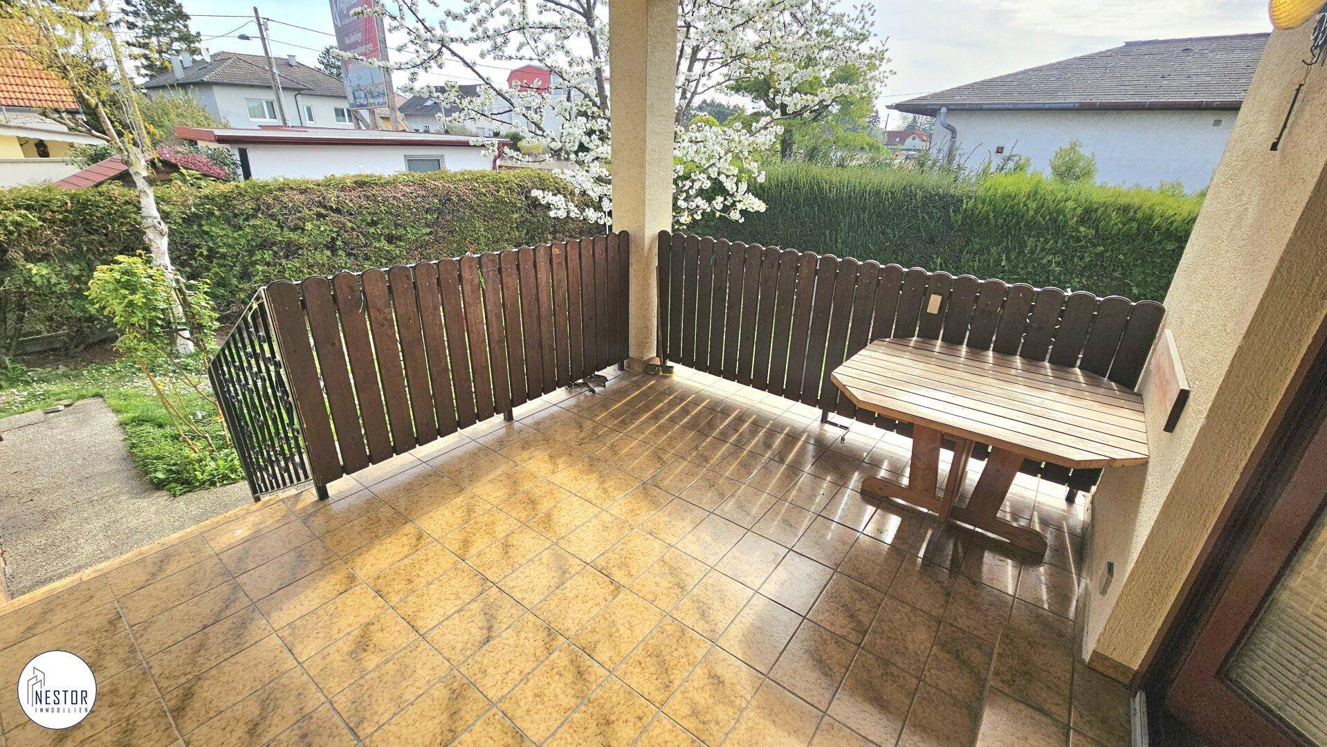 Kleine geflieste Terrasse mit Holztisch und Blick ins Grüne, ideal für Mahlzeiten im Freien.