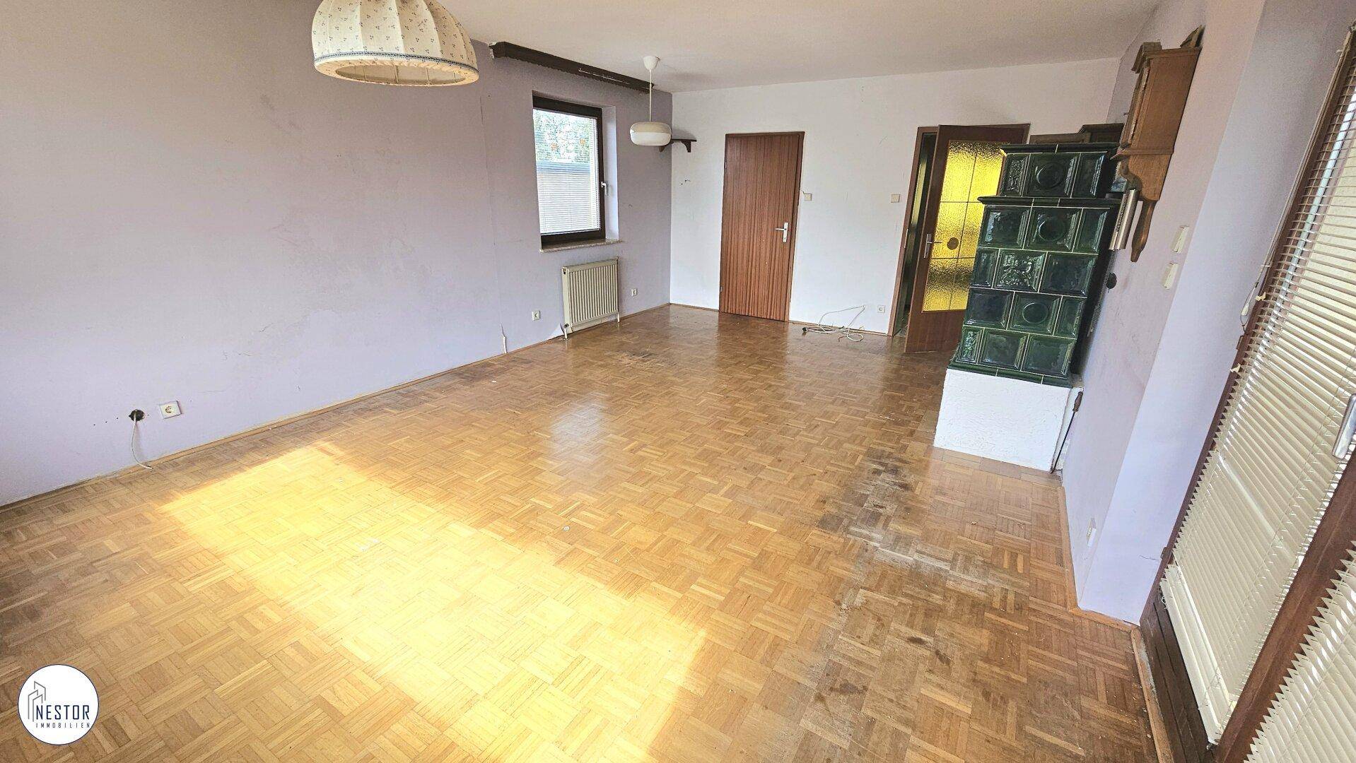 Helles Wohnzimmer mit Parkettboden und traditionellem Kachelofen, bereit zur individuellen Gestaltung.