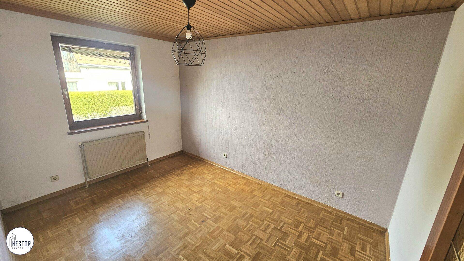 Unmöbliertes Schlafzimmer mit Parkettboden, Holzdecke und Fenster für natürliches Licht.