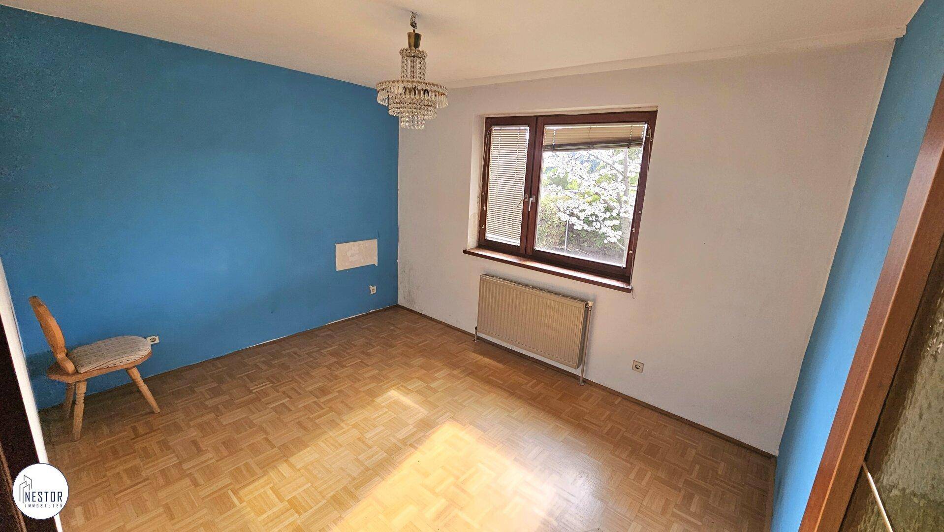 Unmöbliertes Schlafzimmer mit blauer Akzentwand und Parkettboden, bereit zur Einrichtung.