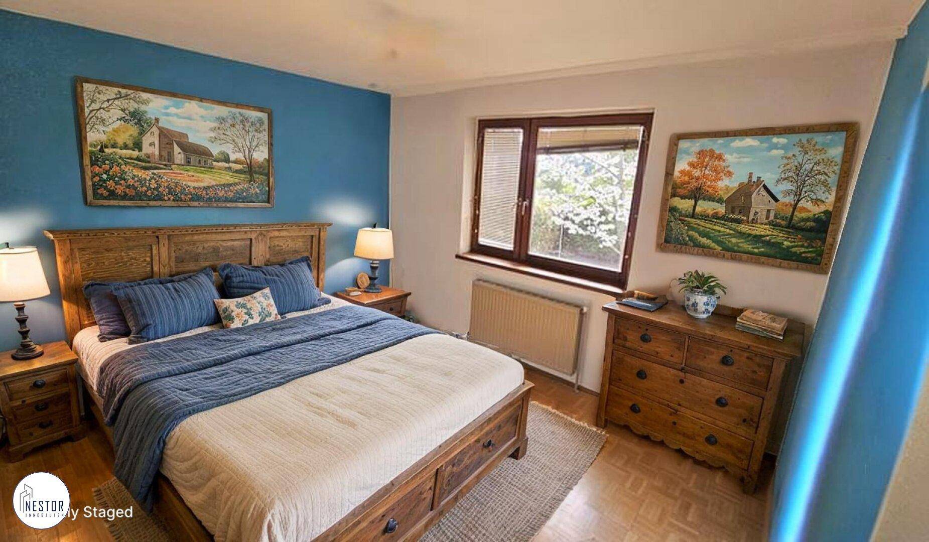 Schlafzimmer mit blauer Akzentwand, Holzbett und Fenster mit Blick ins Grüne.