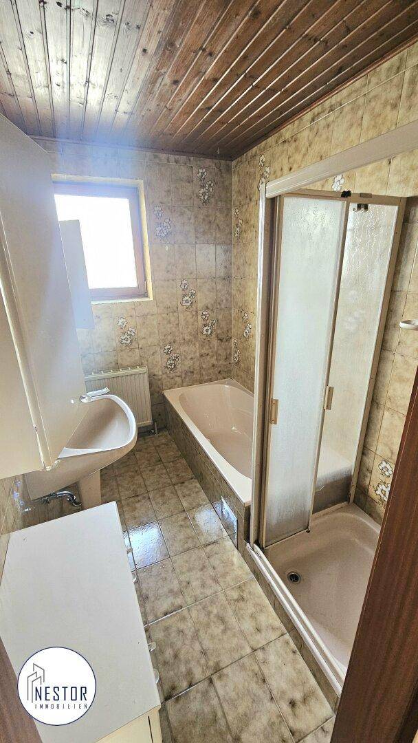 Badezimmer mit Badewanne, Duschkabine, Waschbecken und Fenster, im Stil der 80er Jahre.