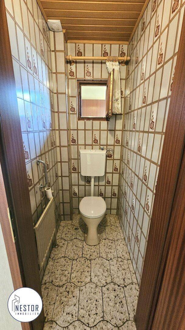 Separate Toilette mit Fenster und gemusterten Fliesen, im Stil der 80er Jahre.