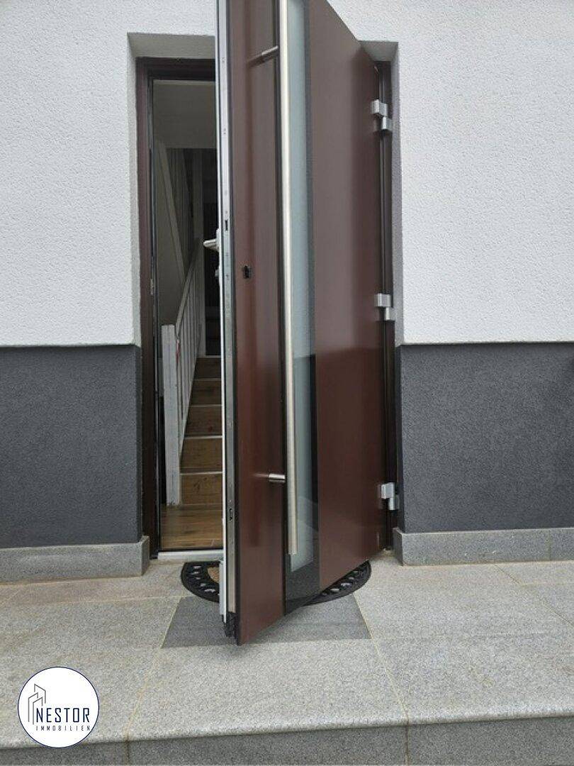 Offene Eingangstür mit modernem Design und Blick auf die Holztreppe im Flur.