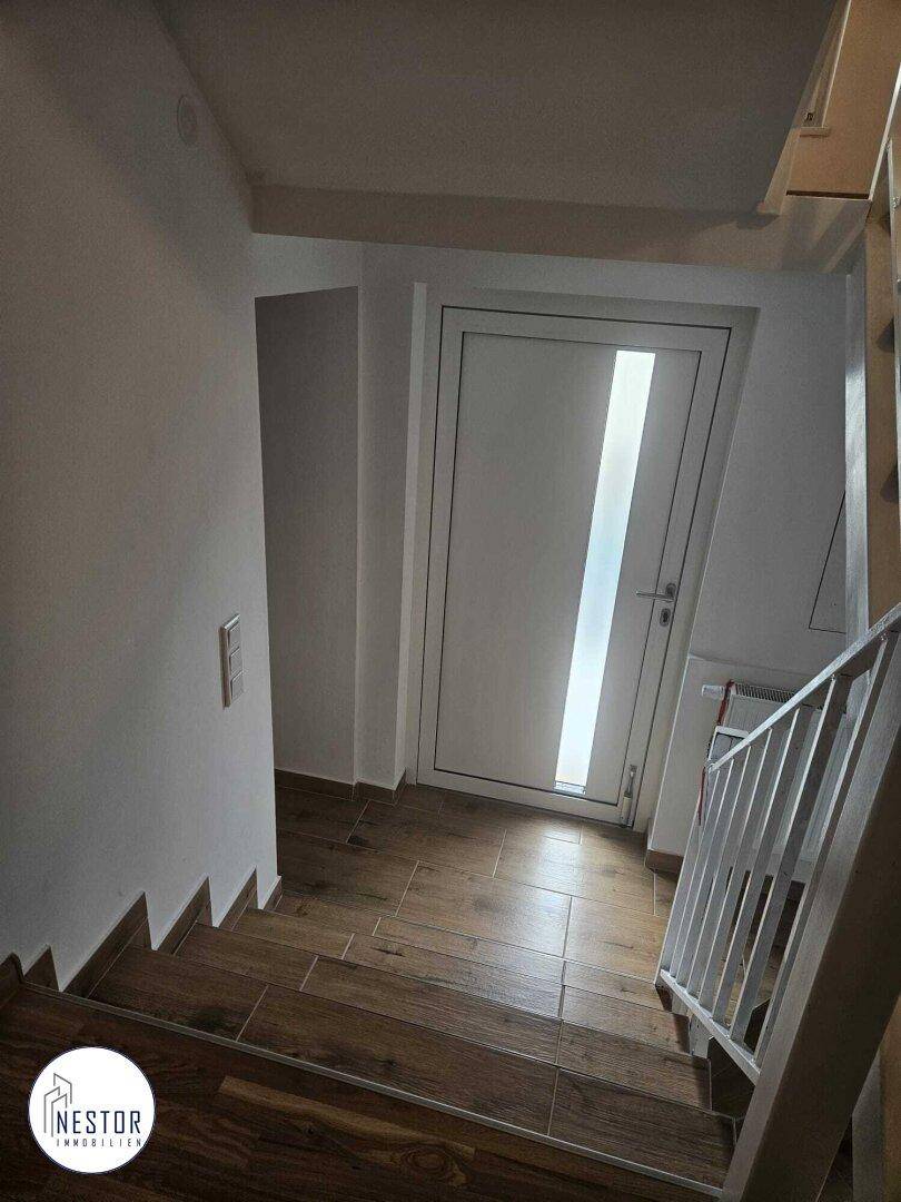 Heller Treppenbereich mit Holzstufen und modernem Türdesign, führt ins Erdgeschoss.