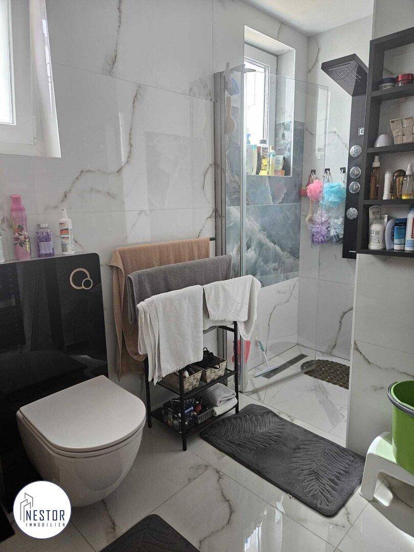 Modernes Badezimmer mit Duschkabine, wandhängendem WC und eleganten Marmorfliesen.