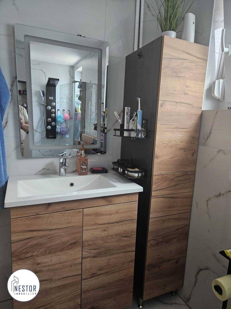 Badezimmer mit modernem Waschtisch, beleuchtetem Spiegel und Holzschrank für Stauraum.