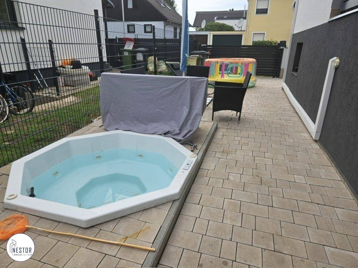 Gepflasterte Terrasse mit Whirlpool und Platz für Gartenmöbel im Außenbereich.