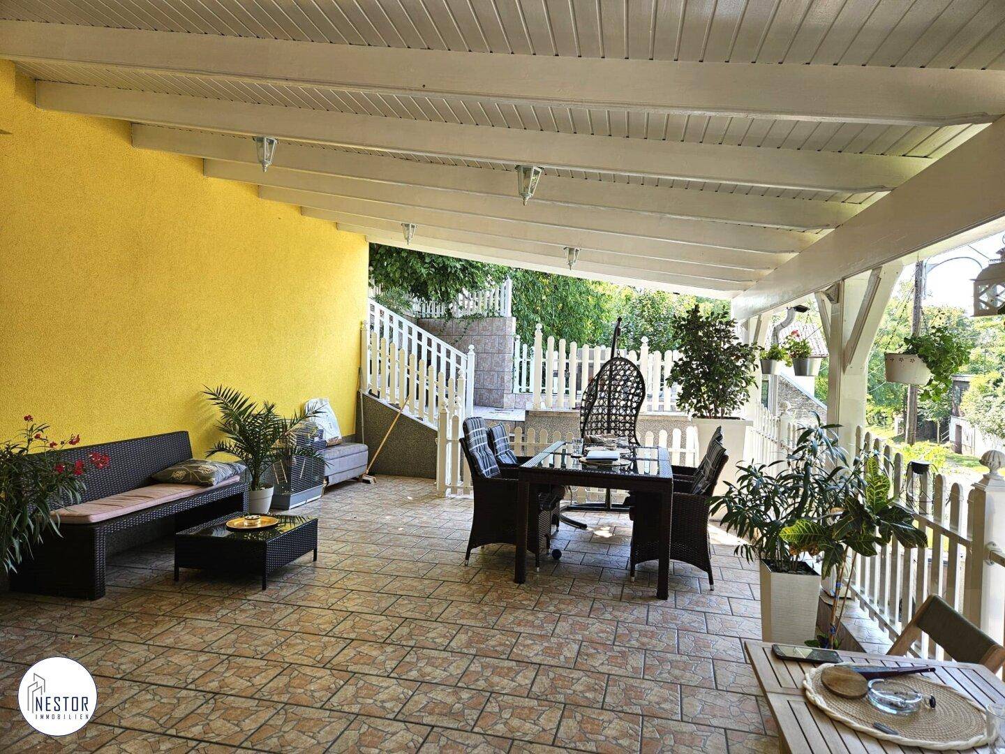 Große überdachte Terrasse mit bequemen Gartenmöbeln und gefliestem Boden, ideal zum Entspannen.