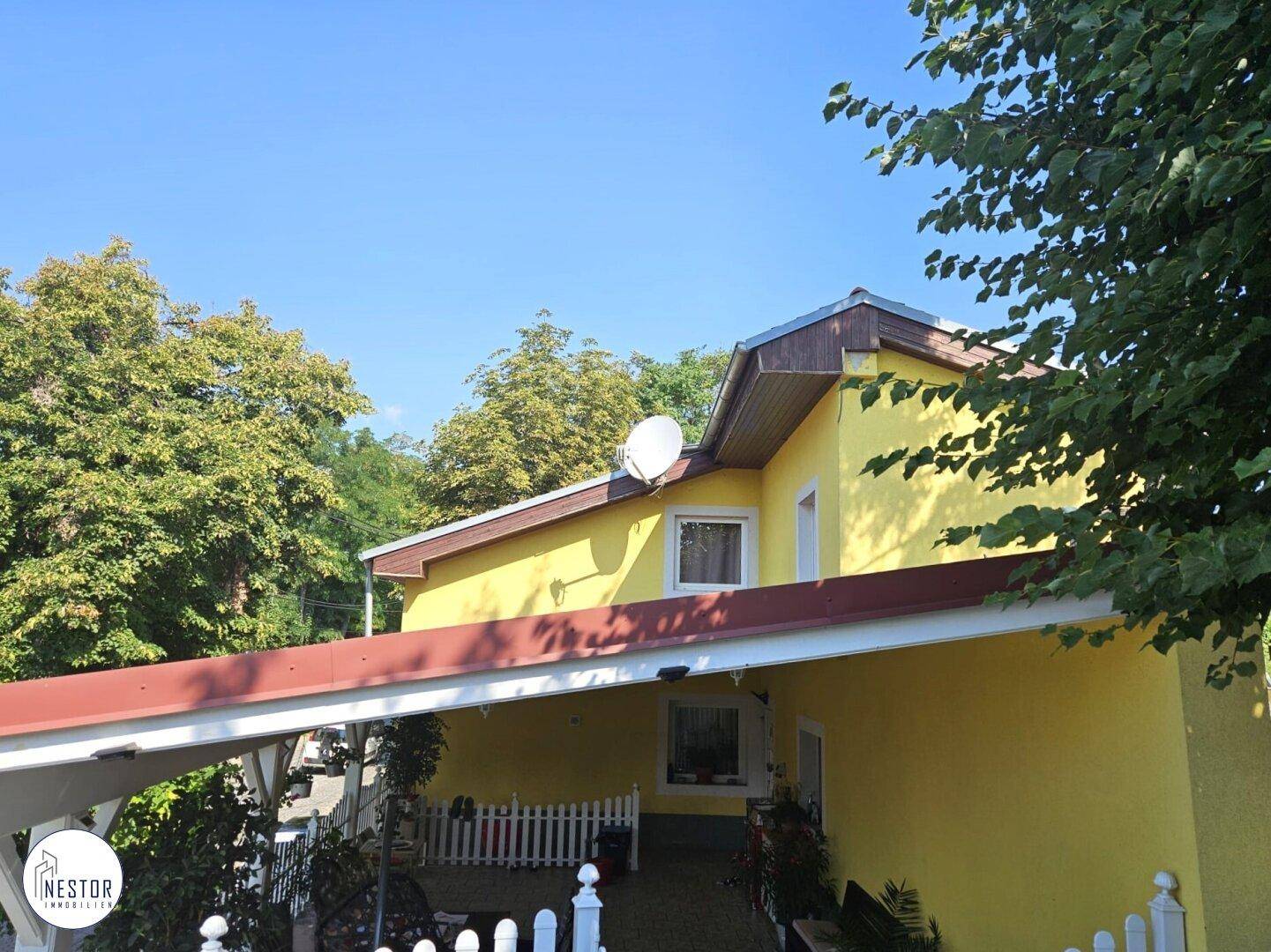 Seitenansicht eines gelben Hauses mit Satteldach und einem überdachten Carport darunter.