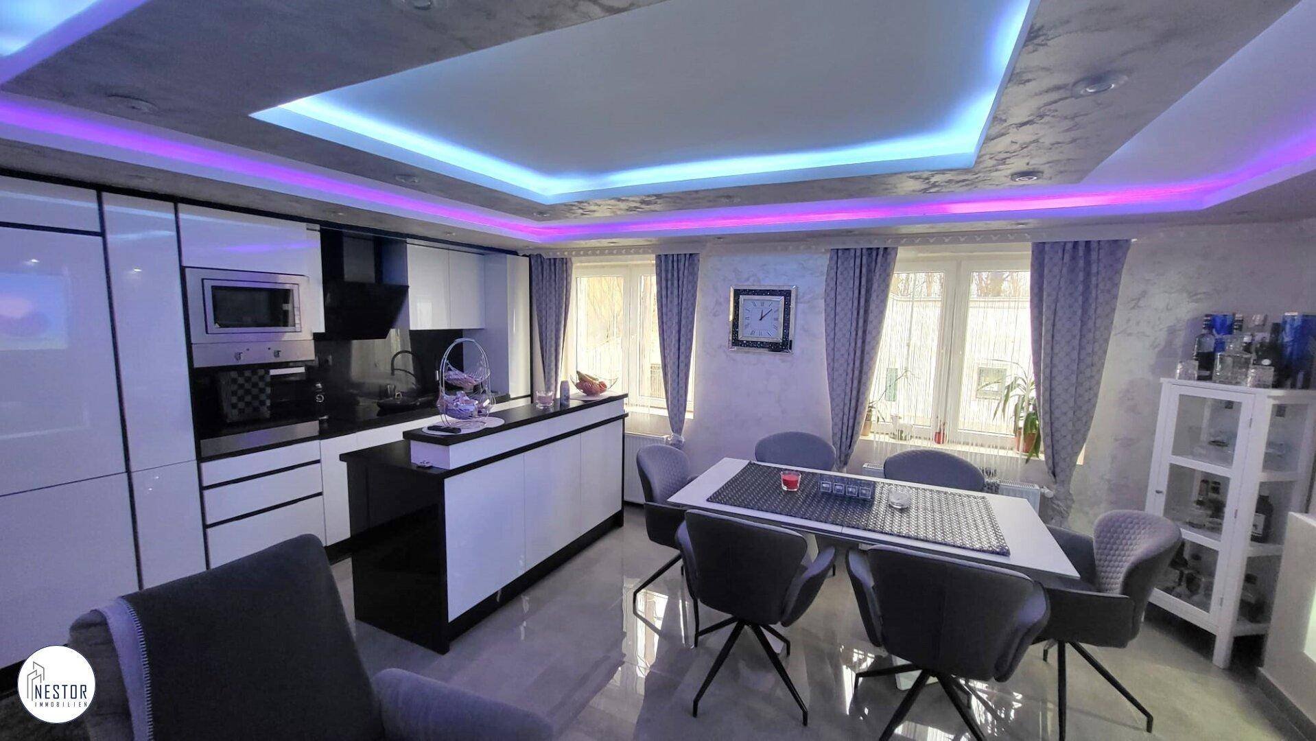 Moderne offene Küche mit Essbereich, Hochglanzfronten und farbiger LED-Deckenbeleuchtung.