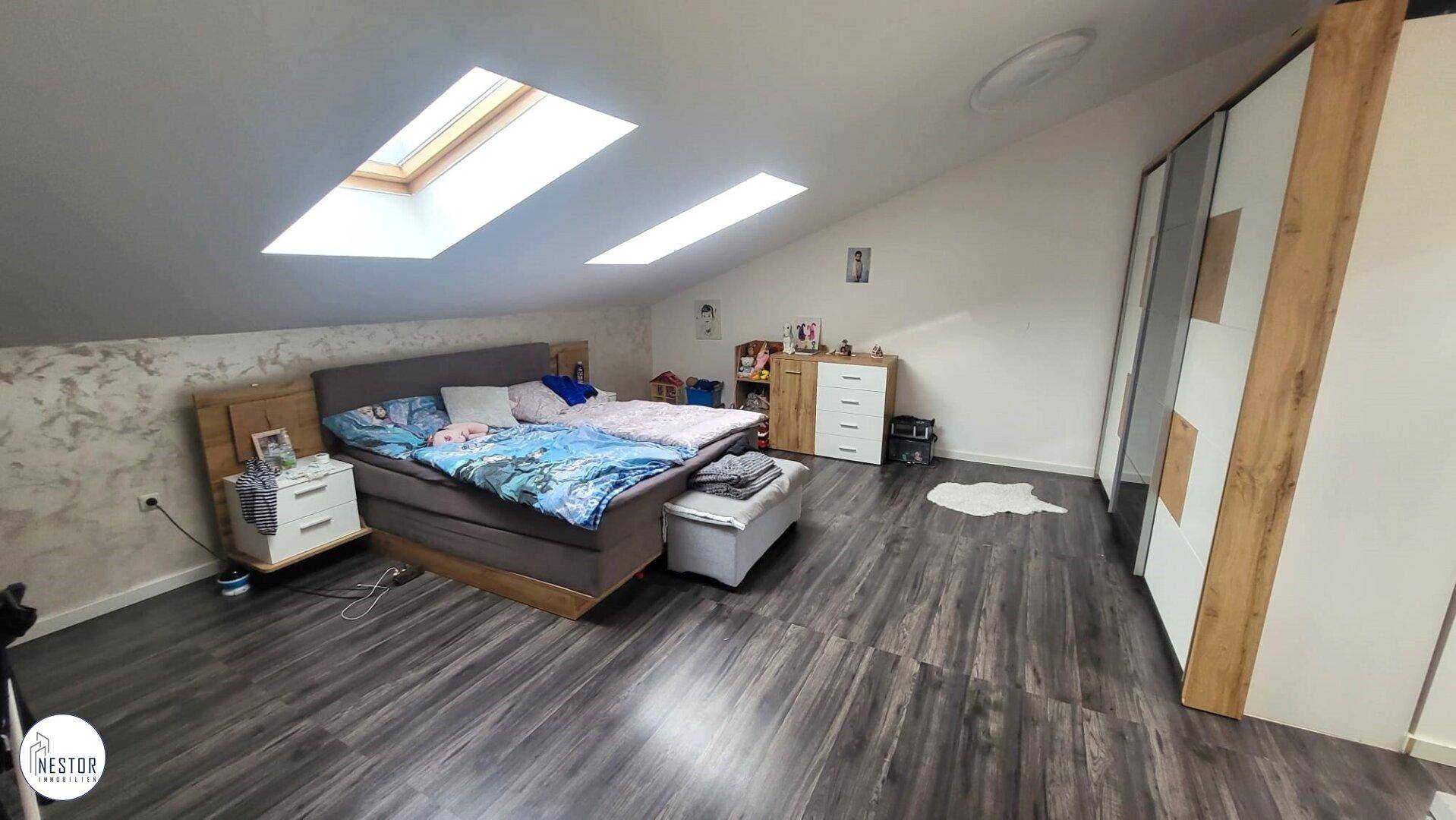 Geräumiges Dachschlafzimmer mit zwei Dachfenstern, dunklem Laminatboden und viel Tageslicht.