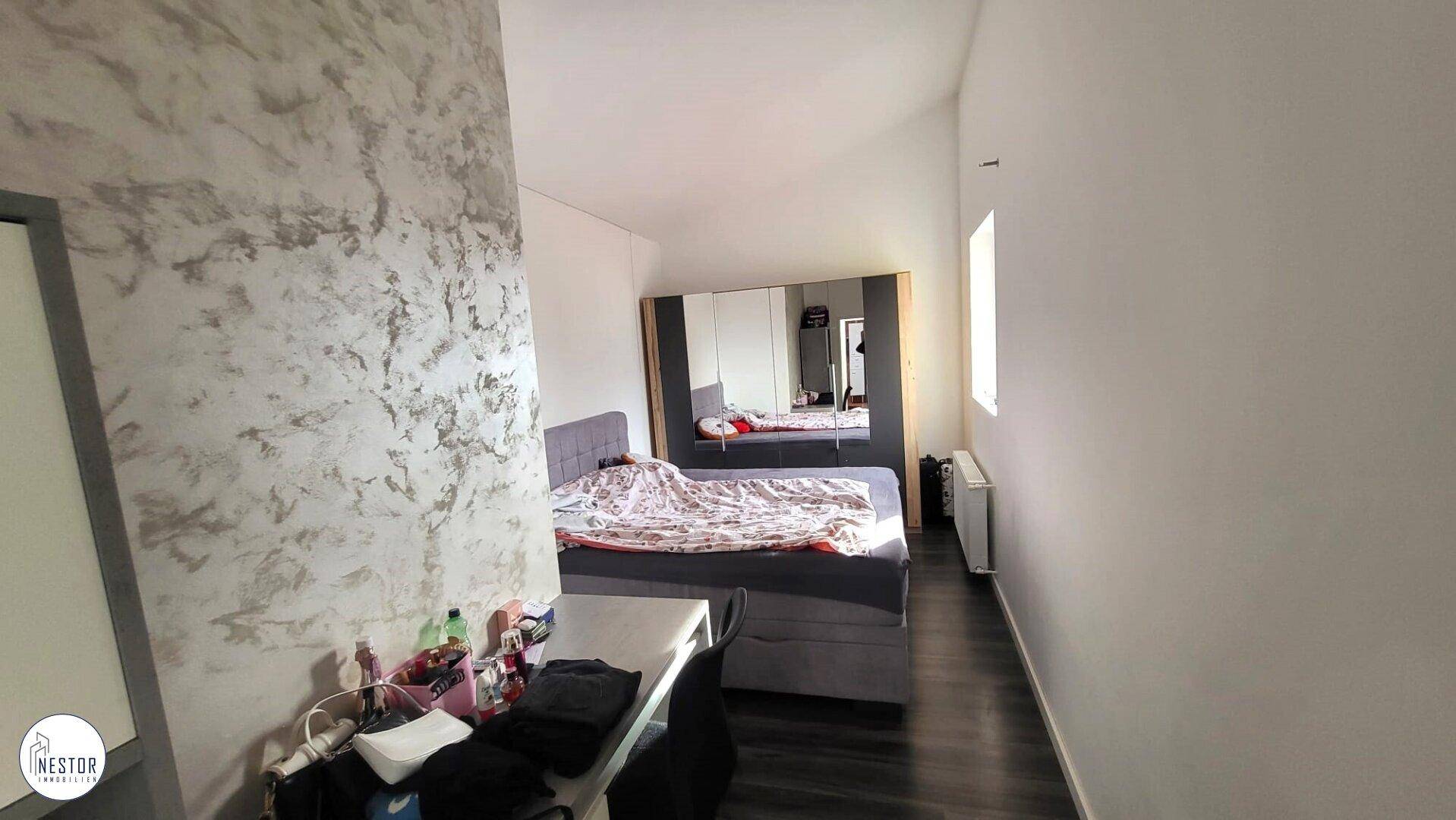 Schlafzimmer mit Doppelbett, Spiegelschrank und dunklem Laminatboden, hell und funktional.