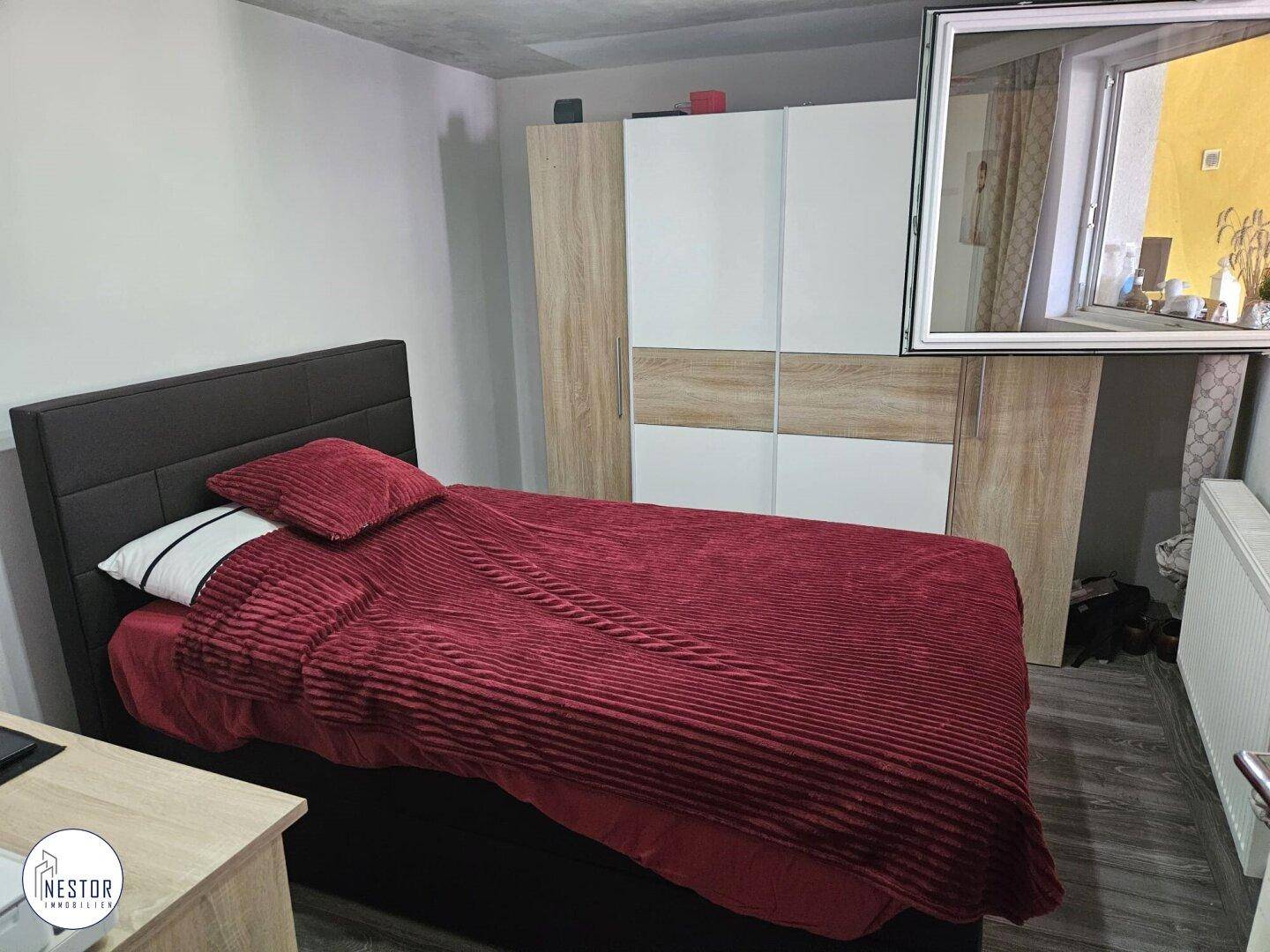 Schlafzimmer mit Einzelbett, Kleiderschrank und dunklem Laminatboden, mit Fensterblick.