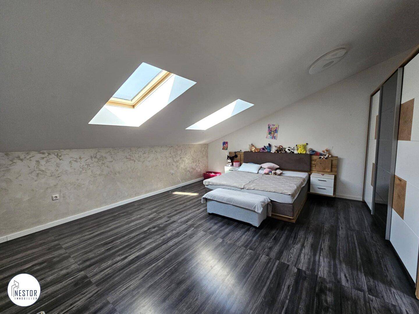 Großes Dachschlafzimmer mit schrägen Wänden, zwei Dachfenstern und dunklem Laminatboden.