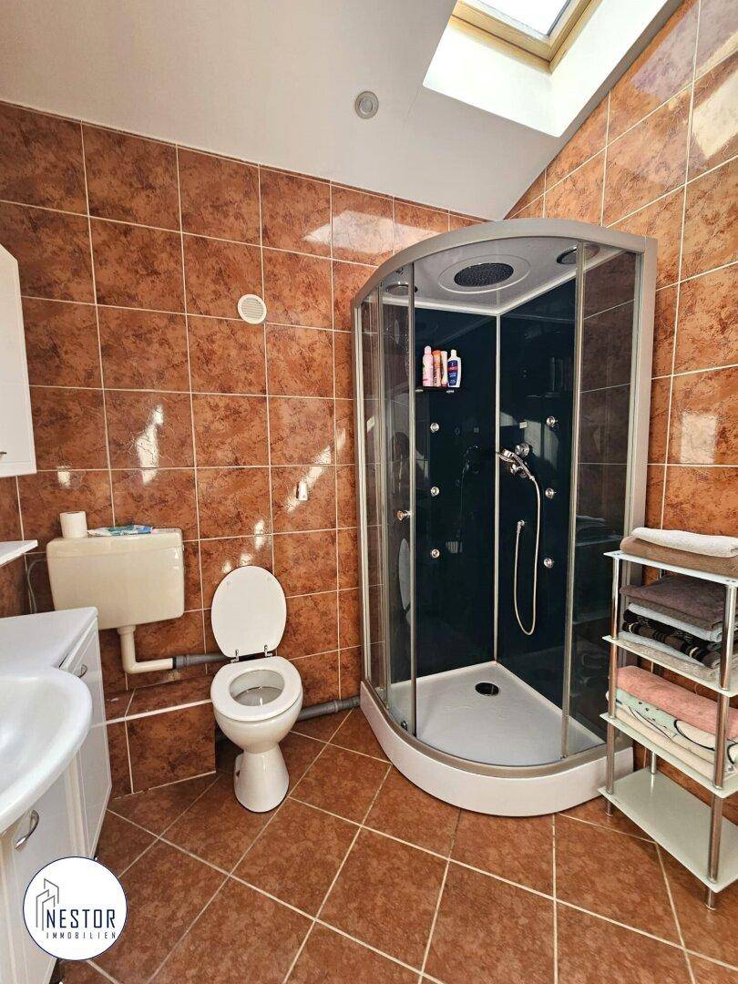 Badezimmer mit braunen Fliesen, moderner Duschkabine und Toilette, hell durch Dachfenster.