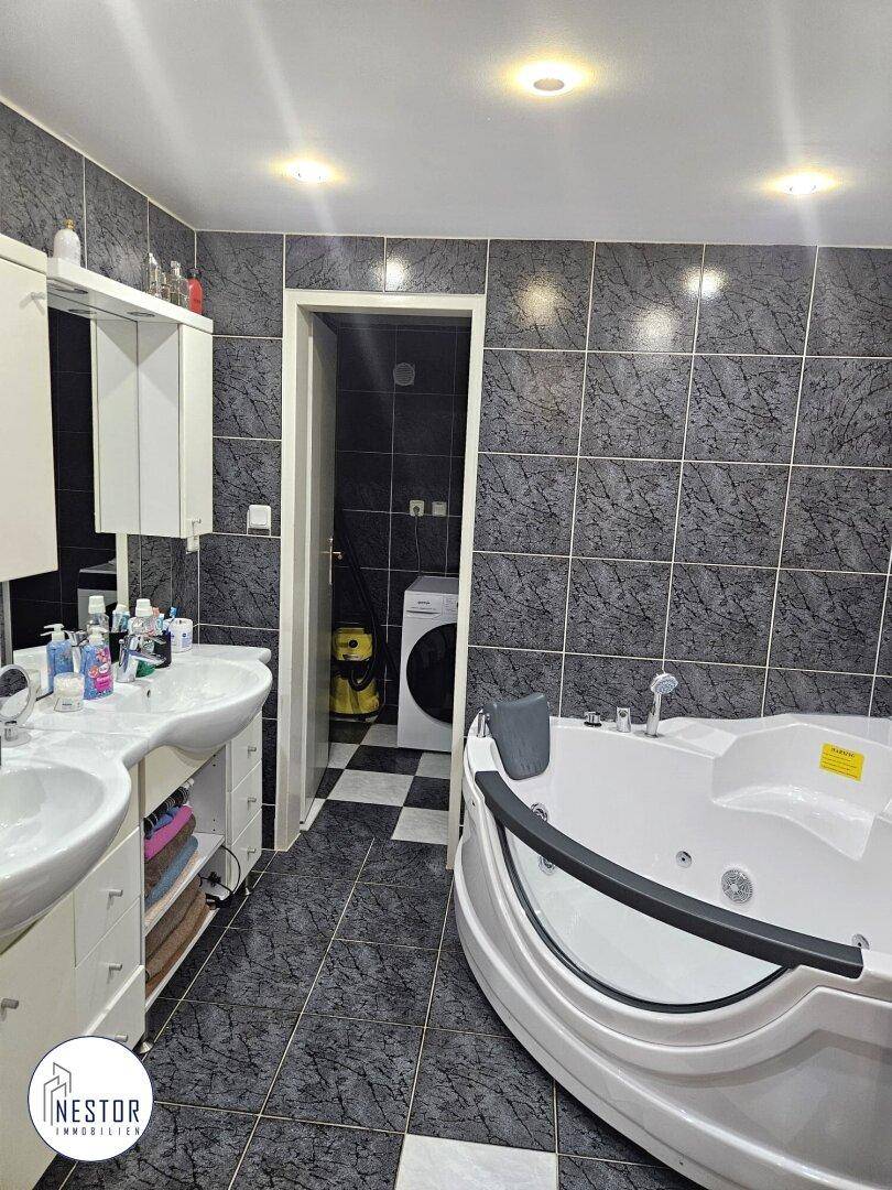Modernes Badezimmer mit dunklen Fliesen, Doppelwaschbecken und einer Eck-Whirlpool-Badewanne.