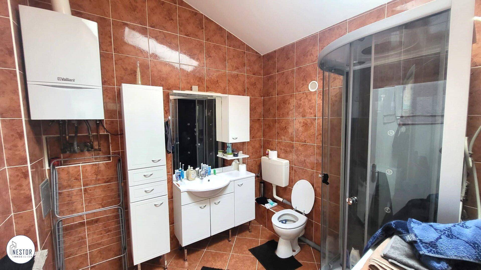 Badezimmer mit braunen Fliesen, Duschkabine, Waschbecken und Wandheizung, funktional eingerichtet.