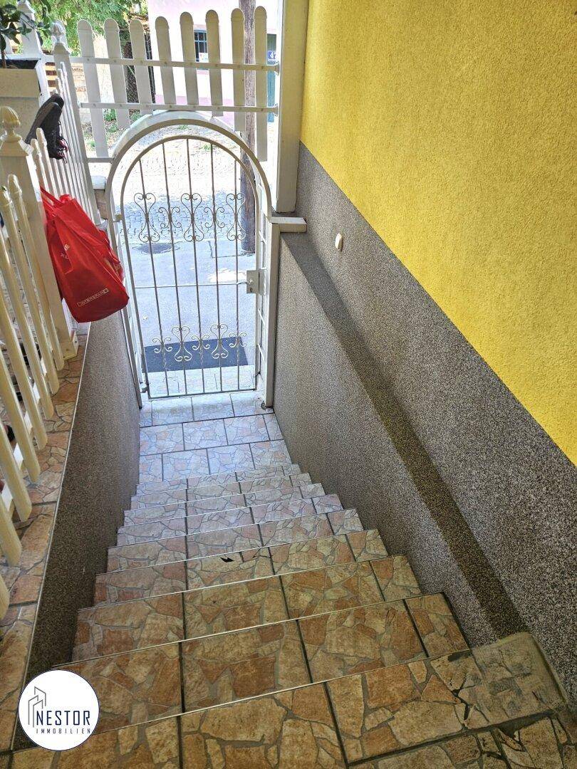 Außentreppe mit gefliesten Stufen und schmiedeeisernem Tor, führt zum Untergeschoss.