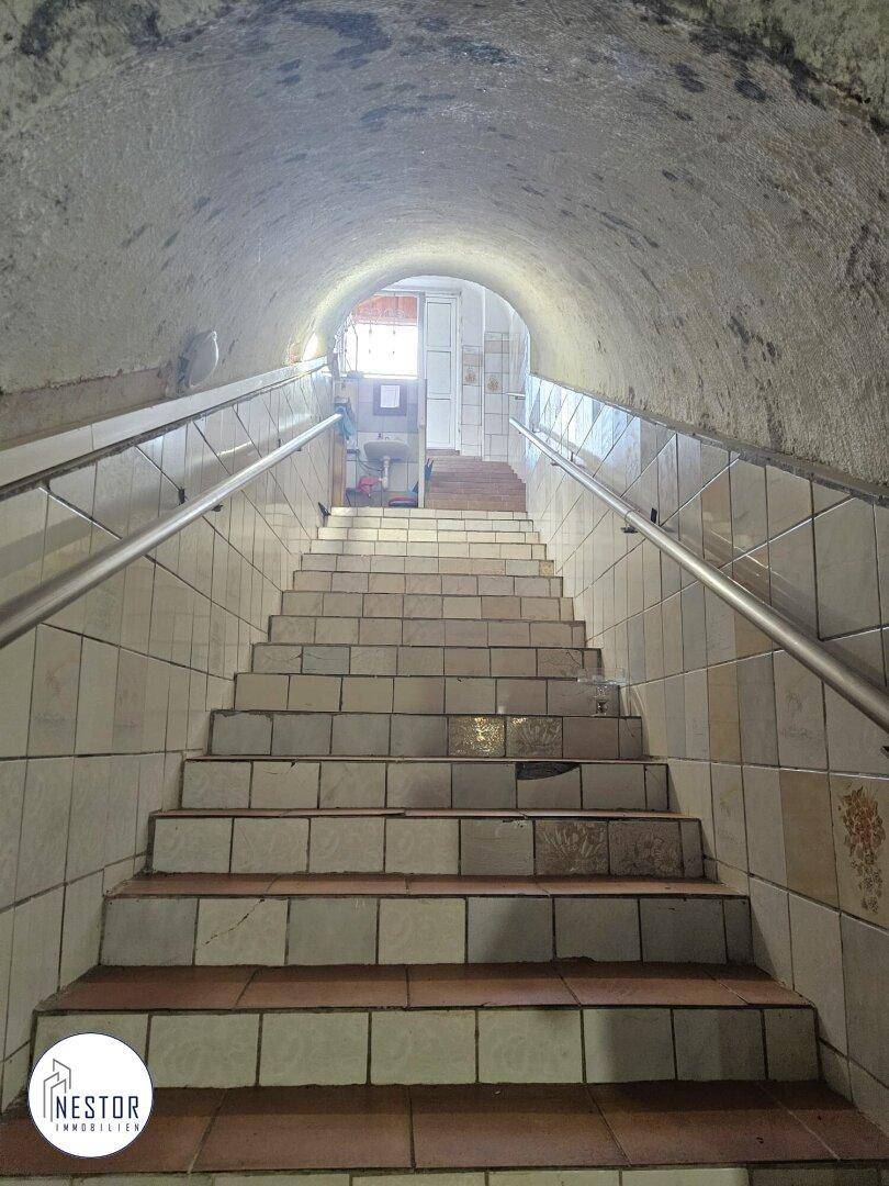 Geflieste Treppe führt in einen gewölbten Kellerraum mit Fliesenboden und Handläufen.