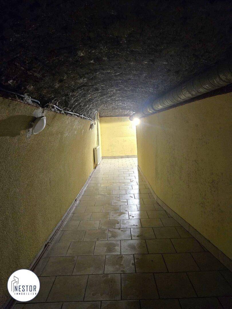 Langer, gefliester Kellerflur mit gewölbter Decke und gelben Wänden, führt in die Tiefe.
