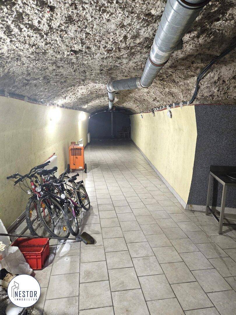 Geräumiger Kellerflur mit Fahrrädern und Lagerbereich, gefliestem Boden und gewölbter Decke.
