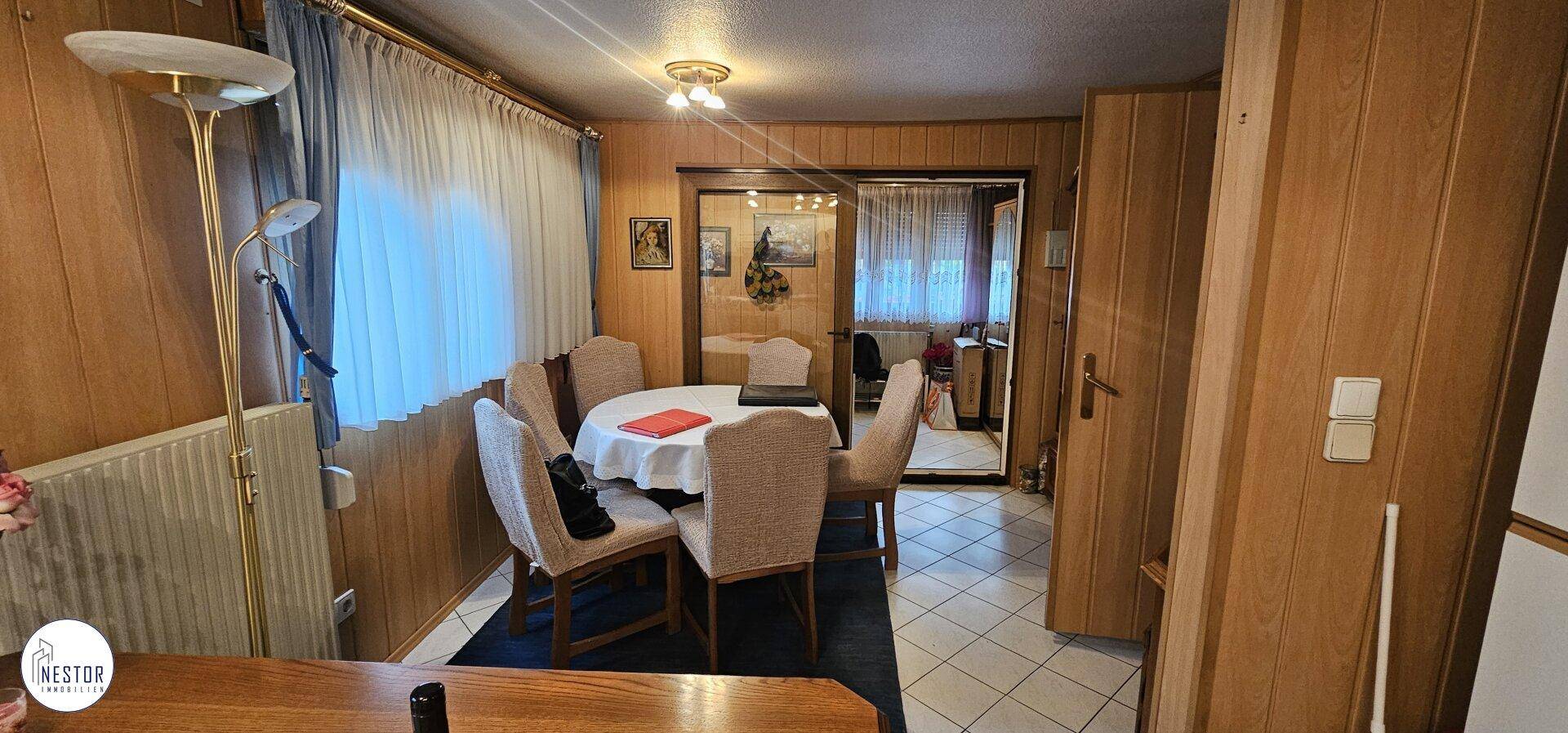 Gemütlicher Essbereich mit Holzwänden, rundem Esstisch und Blick nach draußen durch das Fenster.