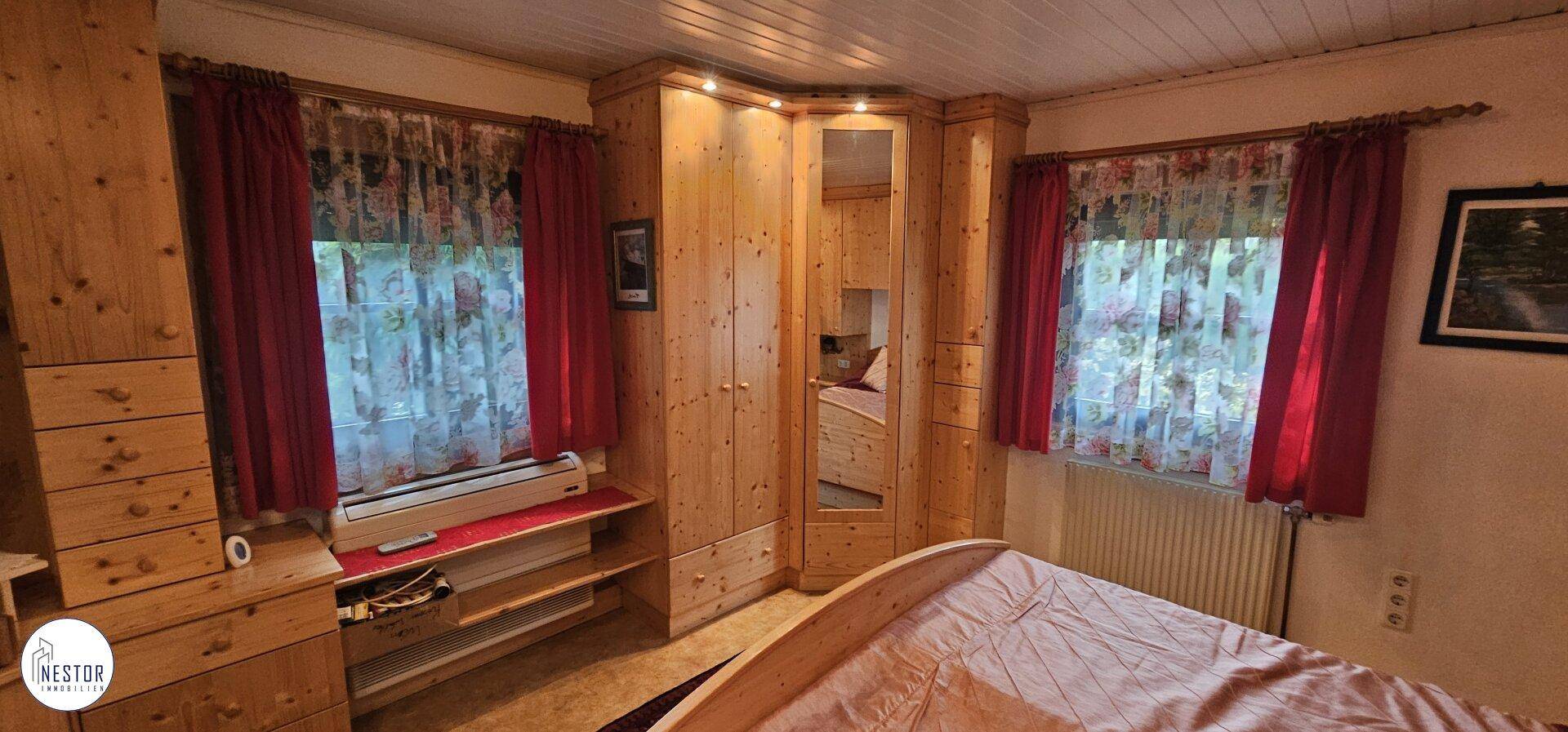 Gemütliches Schlafzimmer mit umfassenden Holzmöbeln, Einbauschränken und einem Heizkörper unter dem Fenster.