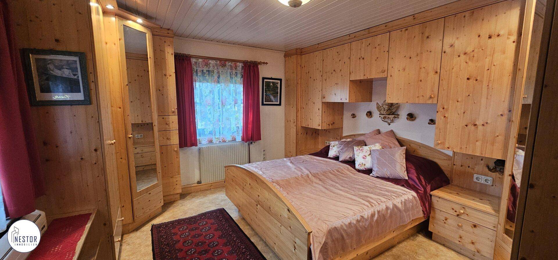 Schlafzimmer mit rustikaler Holzverkleidung, Einbauschränken und einem gemütlichen Bett mit roten Vorhängen.