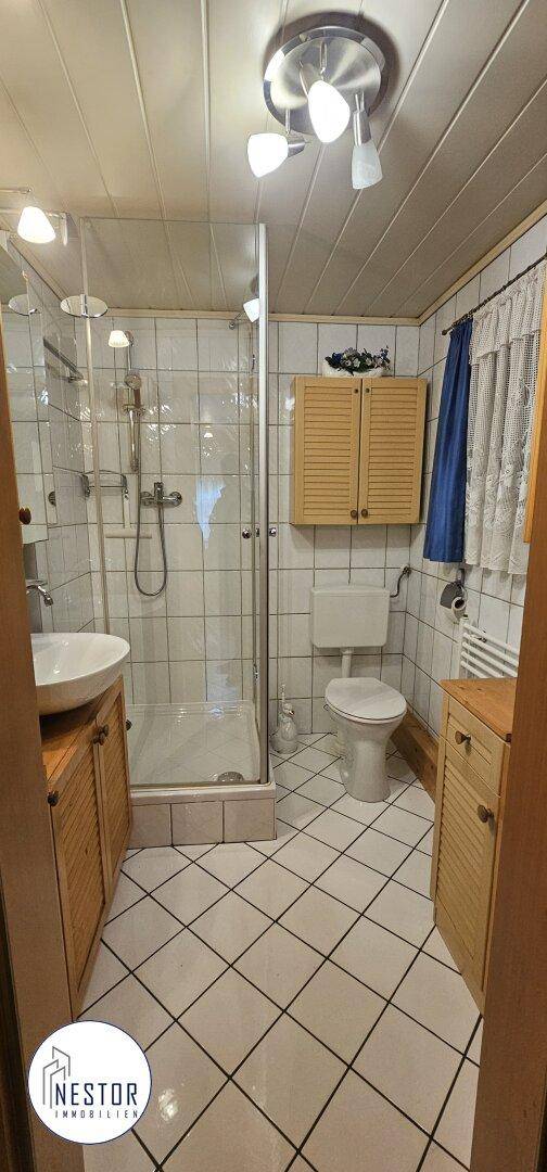 Funktionales Badezimmer mit Duschkabine, WC, Einzelwaschbecken und hellen Fliesen an Boden und Wänden.