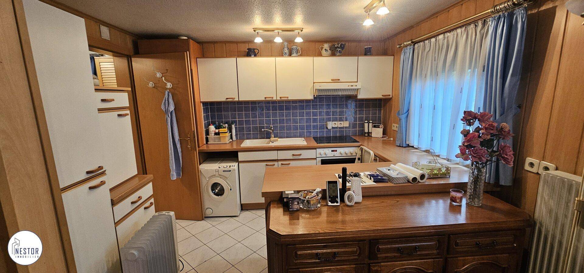 Küche mit weißen Schränken, blauer Fliesenrückwand, Holzarbeitsplatten und integrierter Waschmaschine.