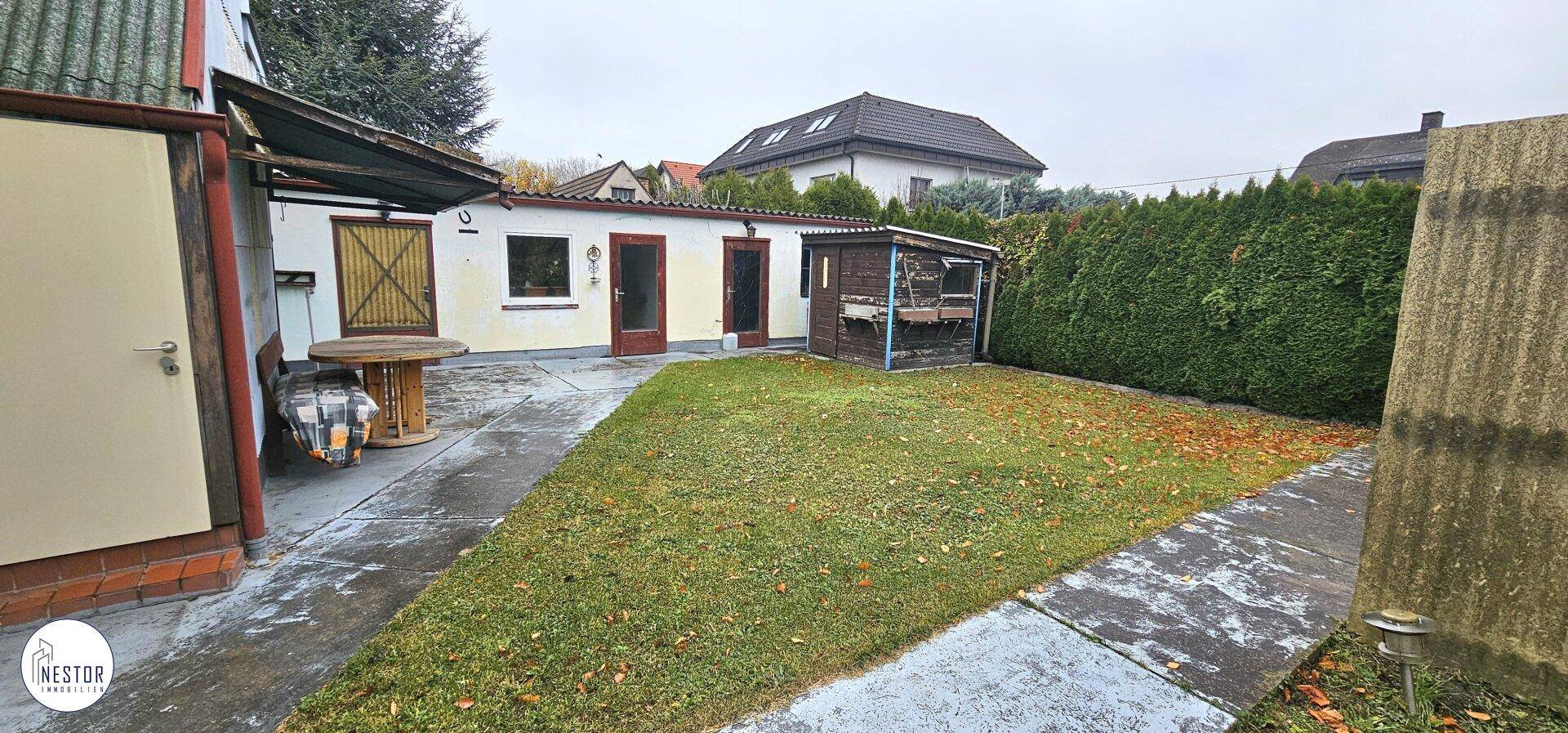 Hinterhofbereich mit Rasen, Hecke und einem kleinen Schuppen neben dem Gebäude.
