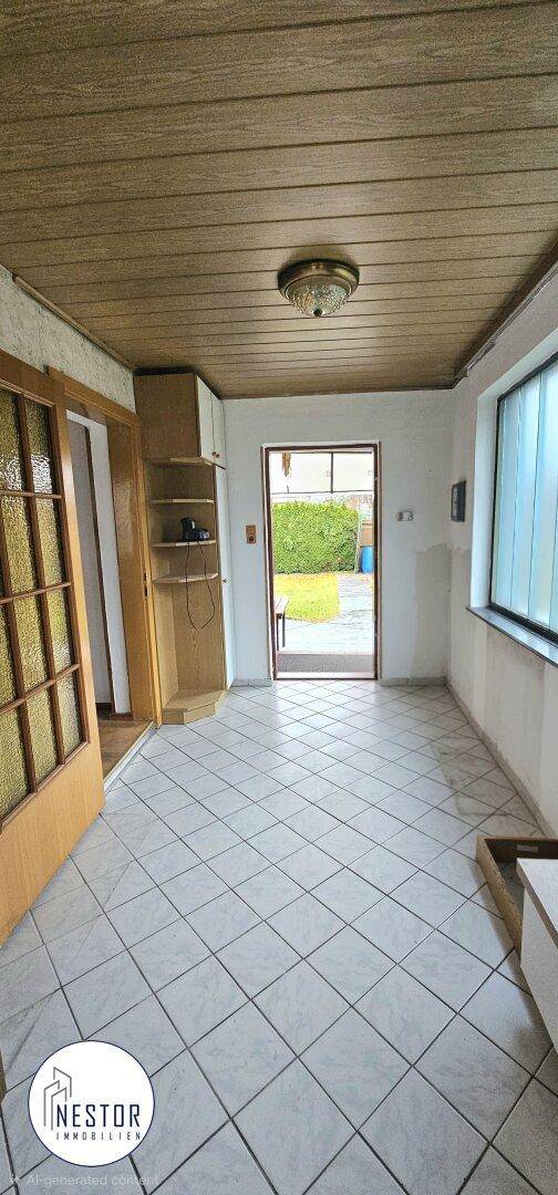 Gefliester Eingangsbereich mit Holzdecke und Blick in den Garten.