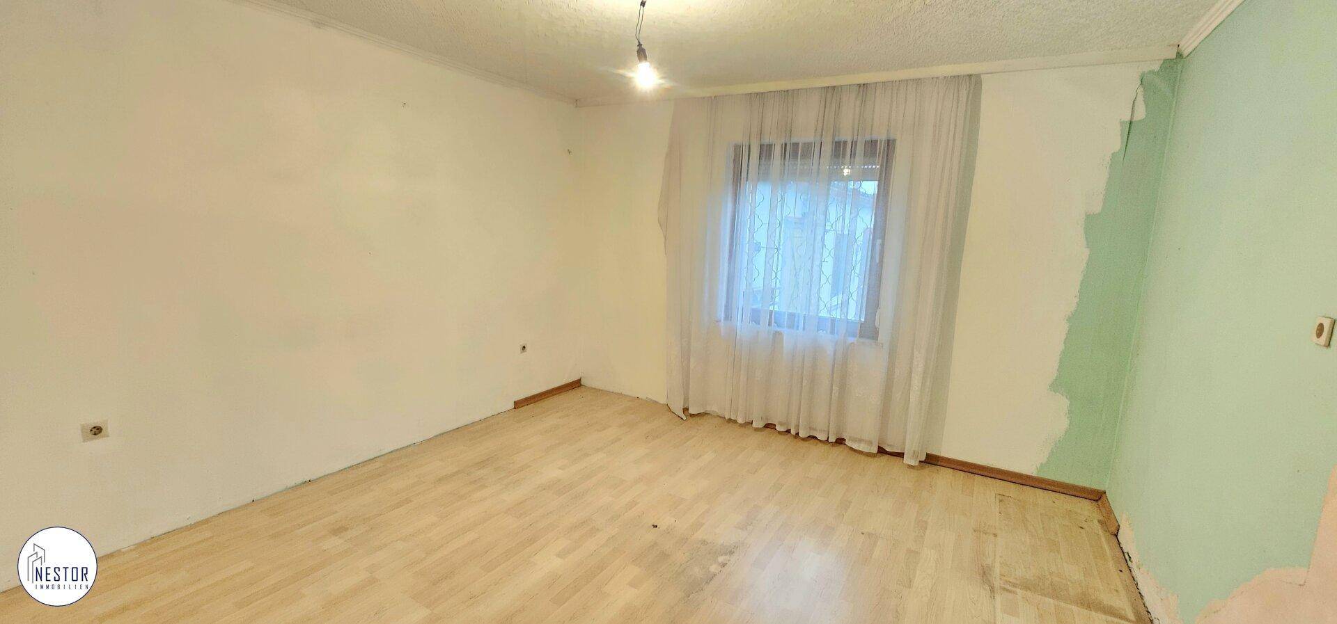 Leerer Raum mit Holzboden und Fenster, bereit für individuelle Gestaltung.