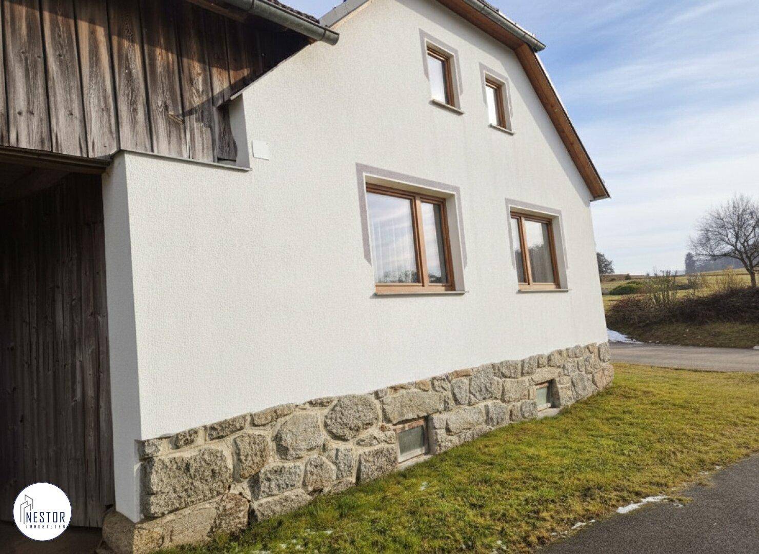 Detailansicht der Hausfassade mit weißem Putz und rustikalem Steinsockel.